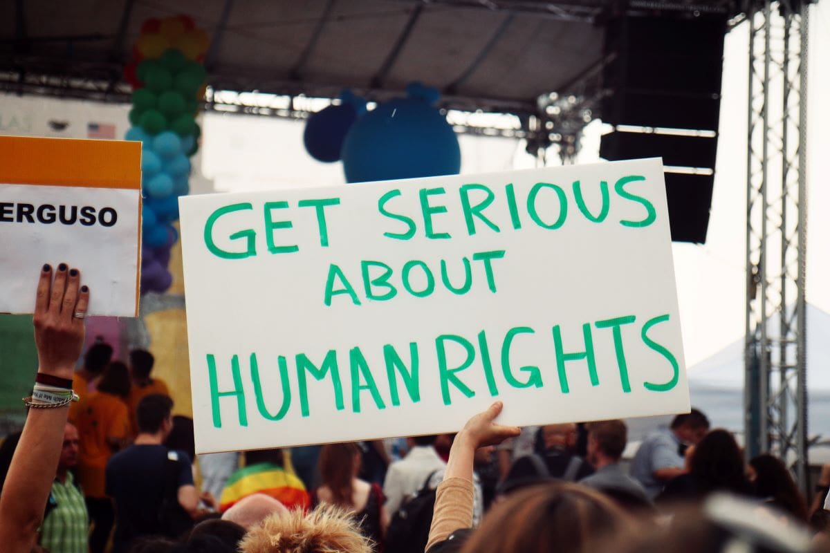 Group of people holding up a sign that says GET SERIOUS ABOUT HUMAN RIGHTS