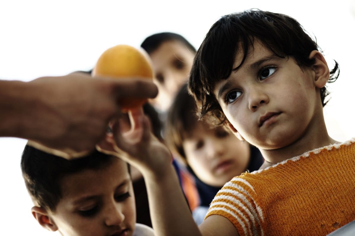 hungry children receiving an orange to eat
