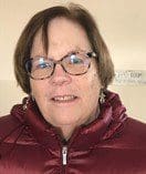 Woman with glasses wearing a red jacket and earrings indoors.