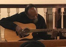 A man playing an acoustic guitar while seated.