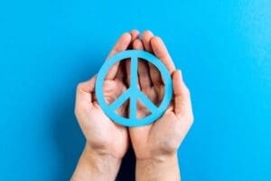 Two hands holding a blue peace symbol against a blue background.