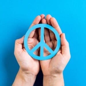 Two hands holding a blue peace symbol against a blue background.