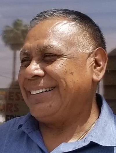 Austin G Nunez is a man with short hair and a blue shirt smiles broadly while standing outdoors.