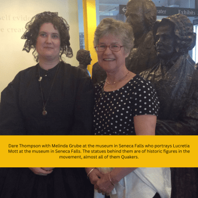 Two women, one in historical attire, stand in front of statues at a museum in Seneca Falls. The statues represent historic figures in the movement.